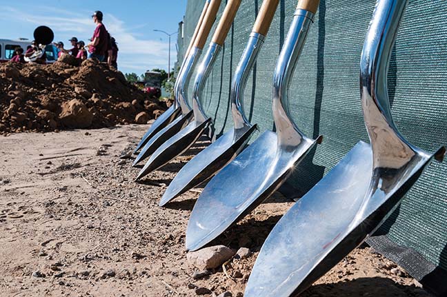 A row of silver shovels lean against a fence