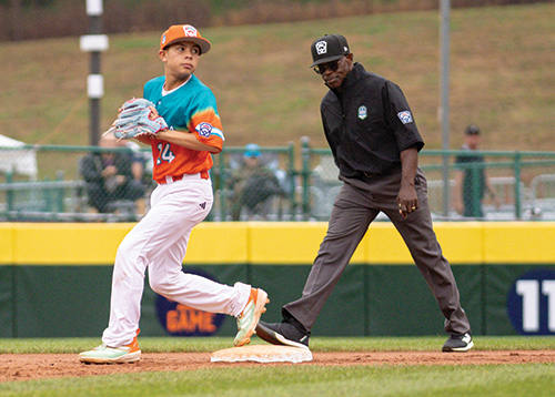 Baseball player stands on a base looking toward the field while an umpire watches nearby on the infield.