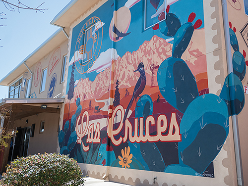 A mural of stamps and a large postcard adorns the side of the Visit Las Cruces building in downtown Las Cruces.