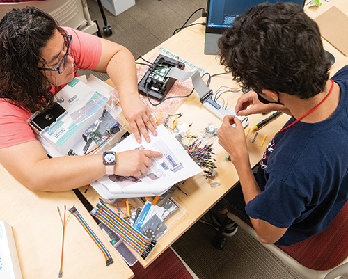 Fretwell, from left, Caylene Romero and Teresa Galvan work on attaching a robotic arm to their robot.